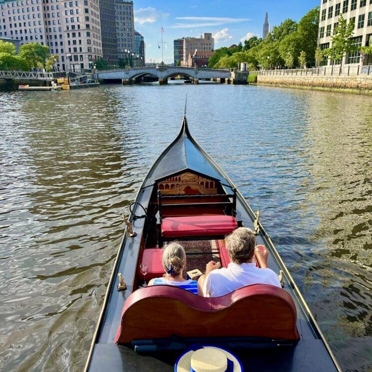 Two passengers in a black La Gondola floating down the calm Providence River
