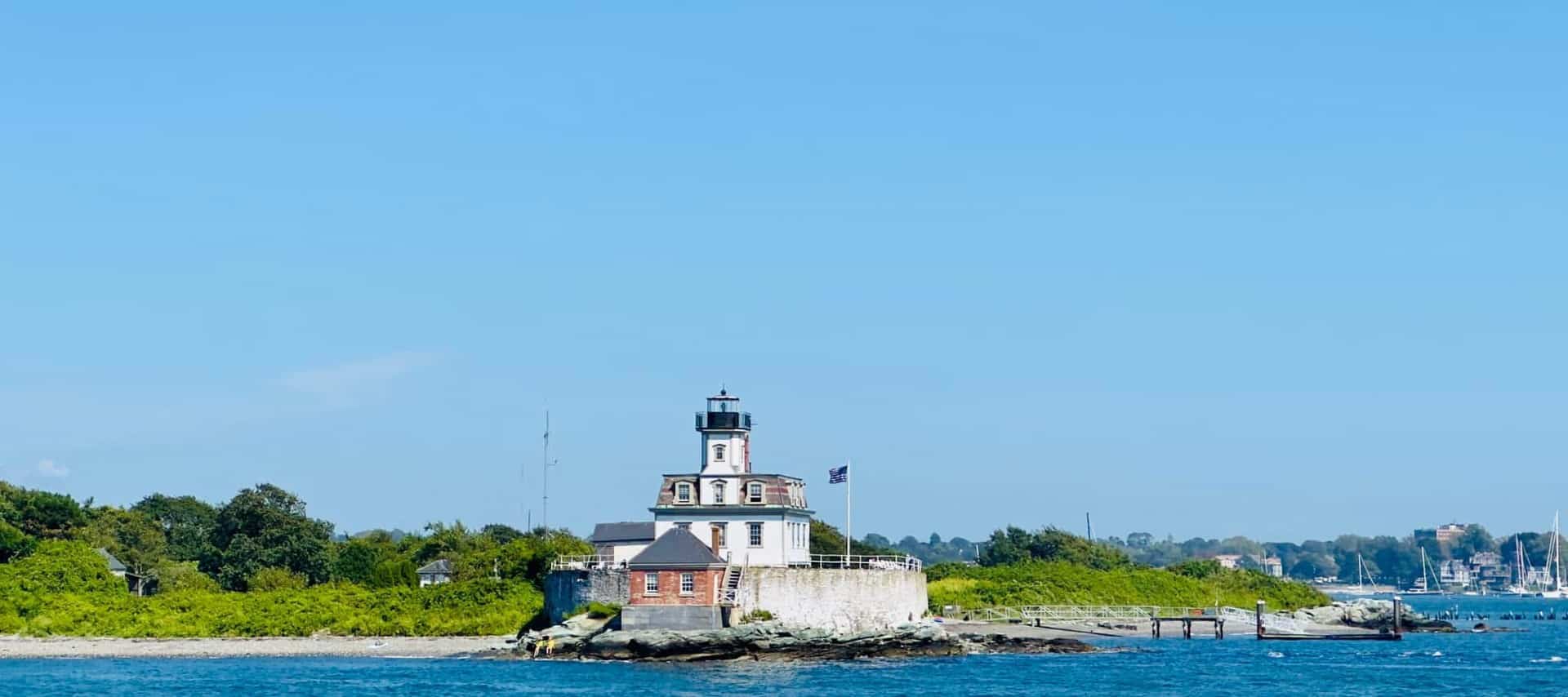 A beautiful stone lighthouse with bright green trees in the background on the mainland