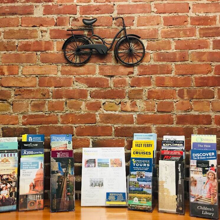Travel brochures on atable backed by a brick wall and a bicycle sculpture.